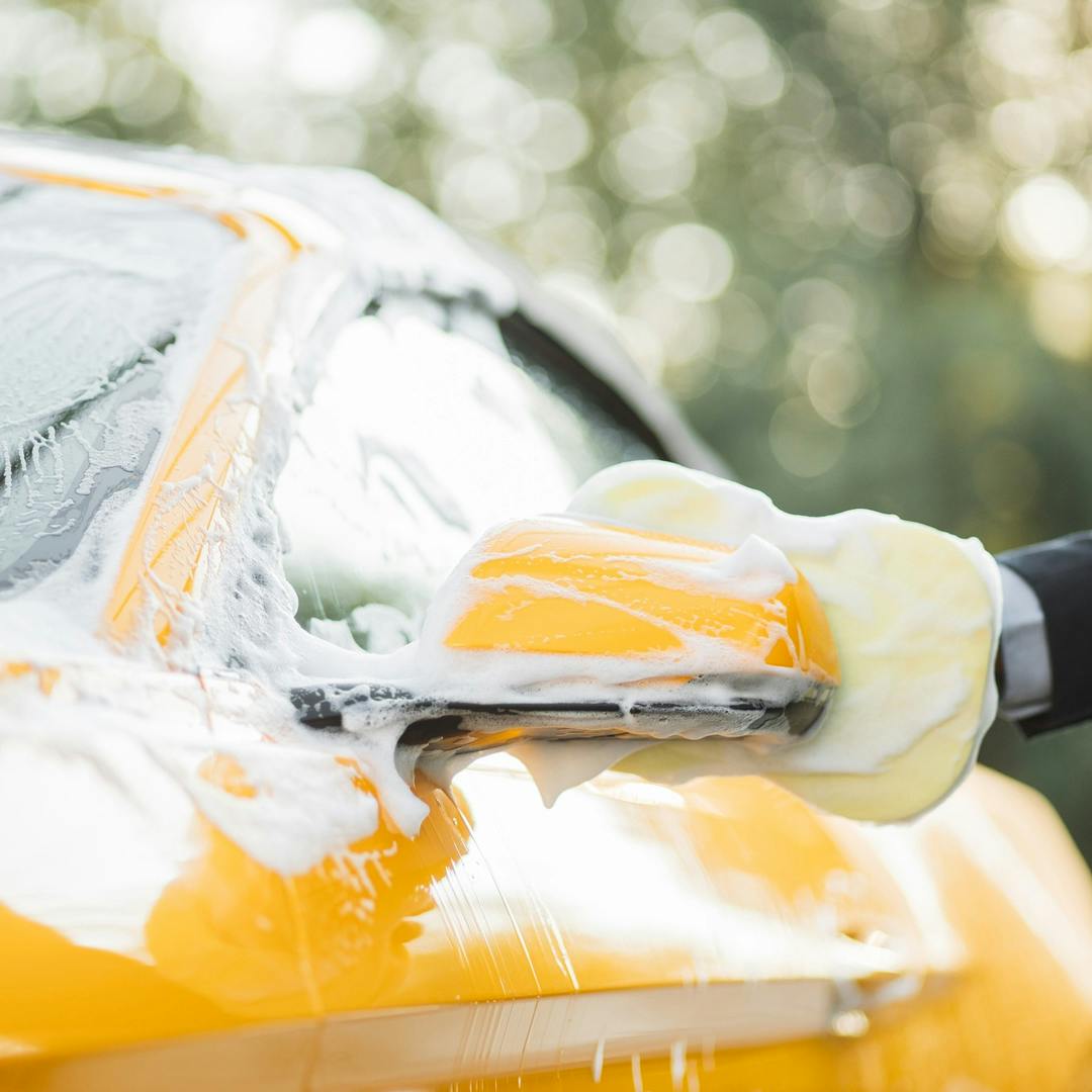 Yellow mustang covered in suds with a man cleaning it with a yellow sponge