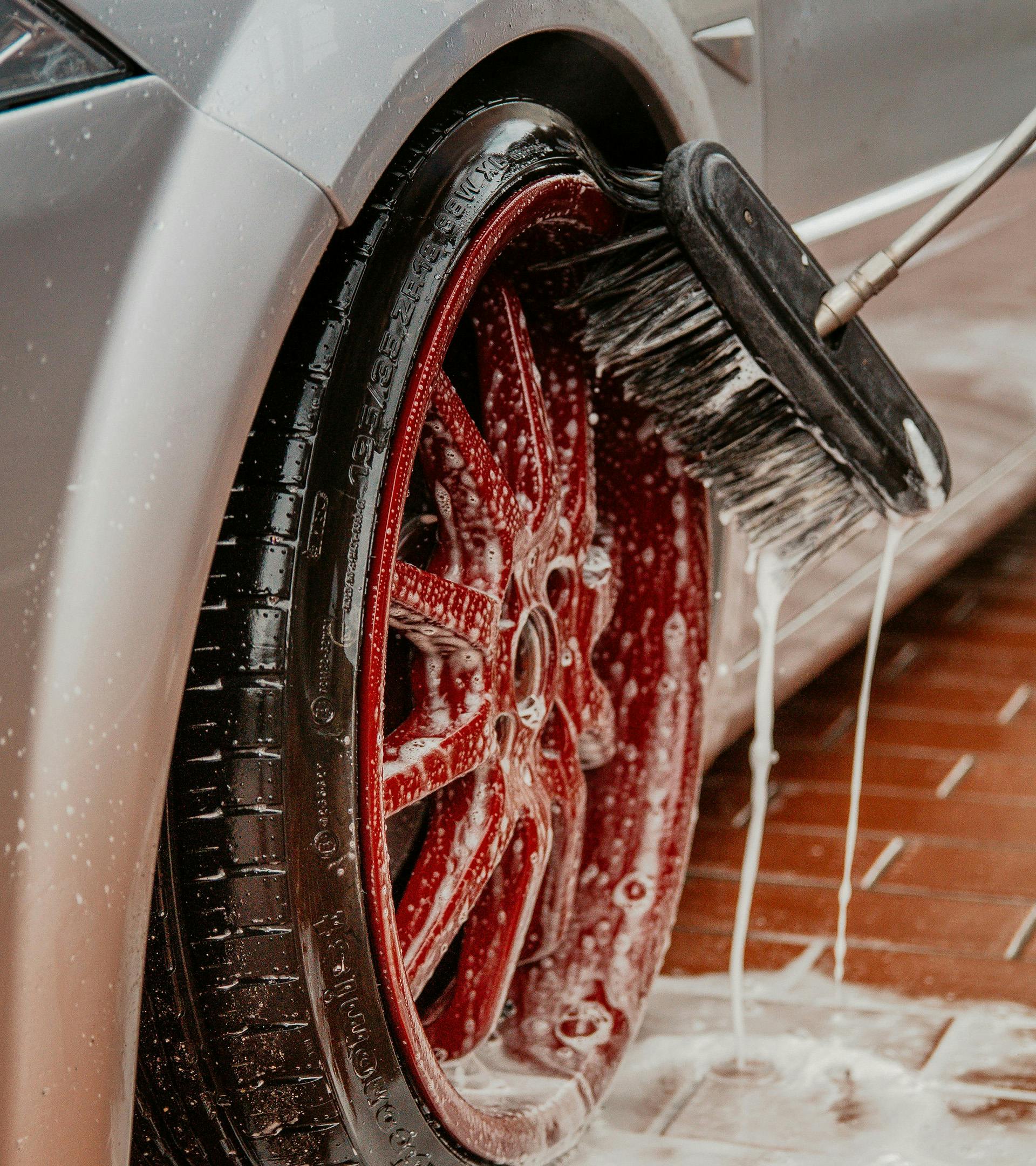 Driver side wheel covered with suds being cleaned by a brush
