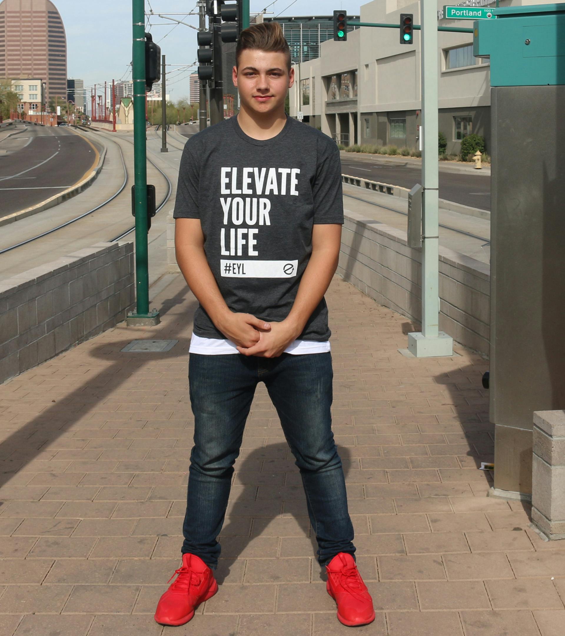 Guy standing wearing a charcoal gray and white Elevate Your Life shirt