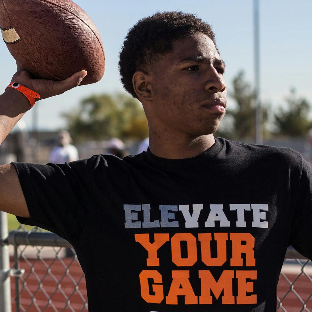 A guy wearing an "Elevate Your Game" shirt throwing a football