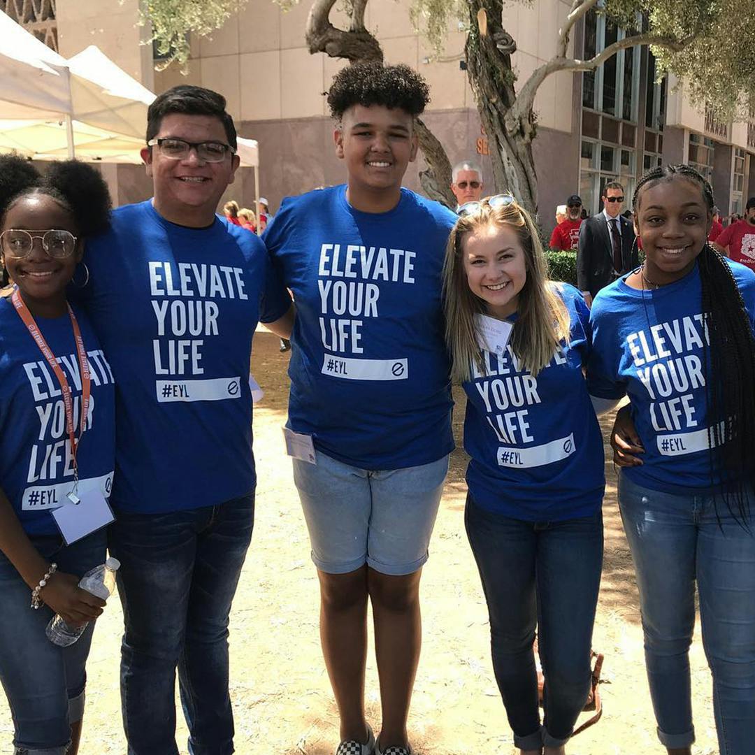 A group of teens, 3 girls and 2 guys, wearing blue and white Elevate Your Life  shirts