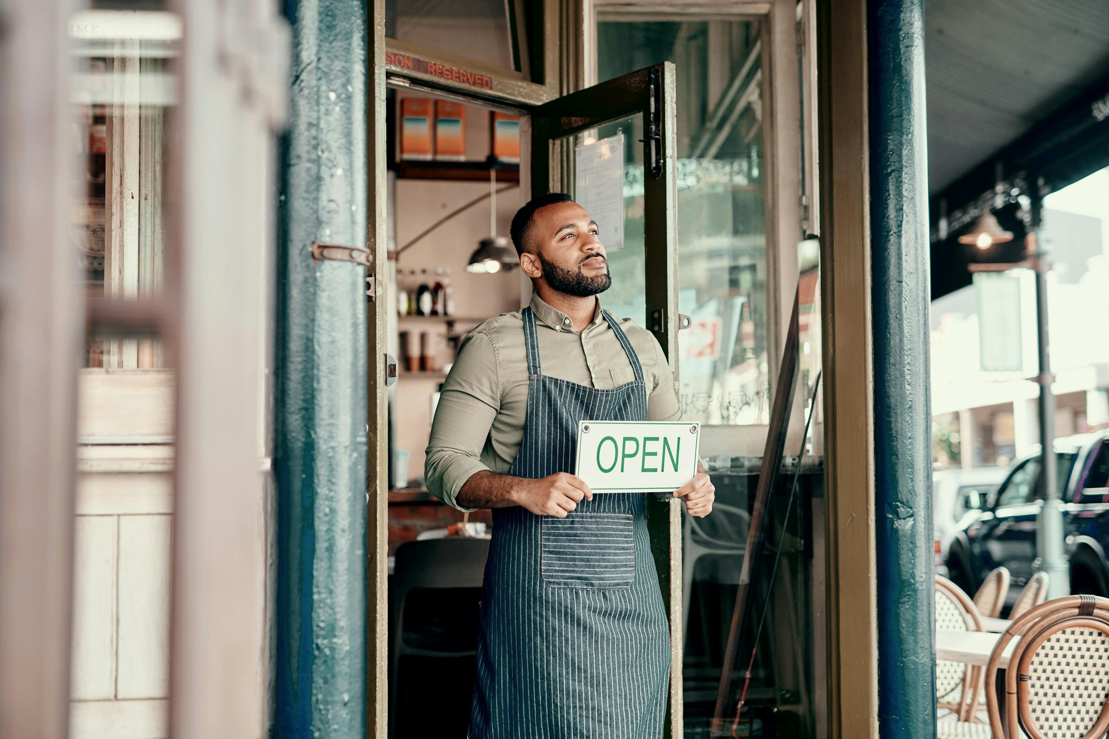 Black man standing outside of his business holding an open sign