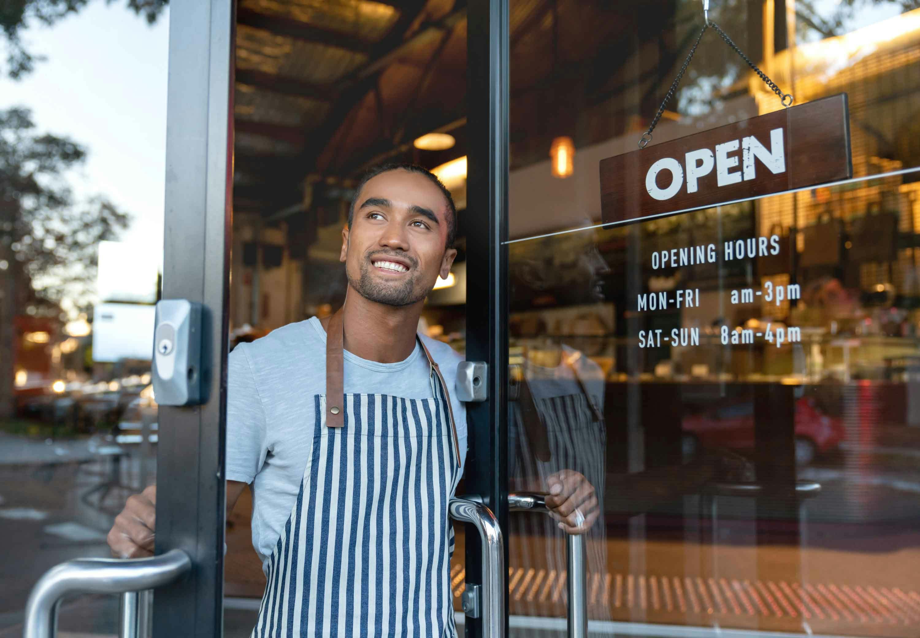 Business owner looking outside door with an open sign and opening hours.