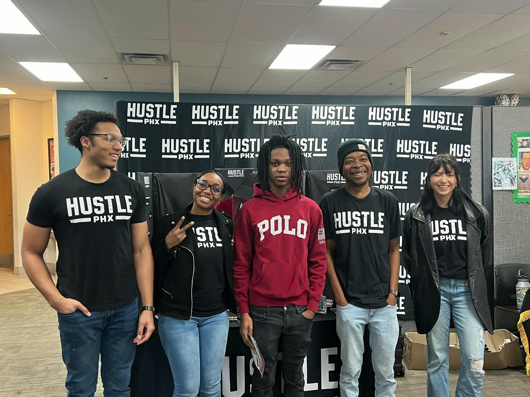 Group of 5 people smiling wearing Hustle PHX shirts